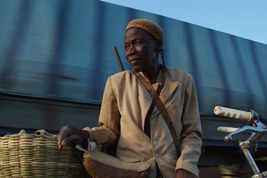 Donsow, traditional hunter on bicycle, truck passing behind, still in Mali