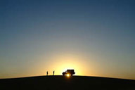 Land Rover on dune, sun sets behind.