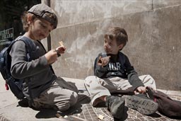Twin boys sitting on pavement and eating chocolate ice cream.