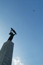 Citadella communist statue and small aircraft in blue sky.