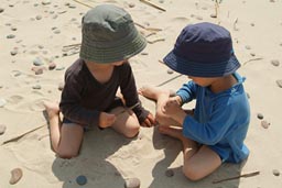 Boys in hats on Latvian beach watch a bug on a stick.