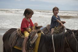 Boys are riding horses on Pacific Beach.