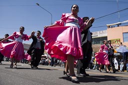 Ladiesin rose, men in black, couples dance down the street o Arequipa Day.