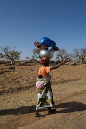 Sanga. Dogon woman, baby on back, carrying heavy head load.