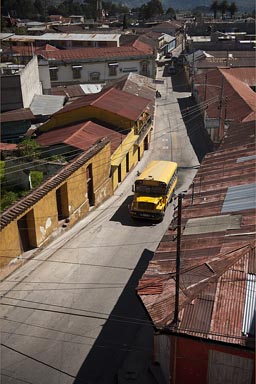Steep street, rusty tinned roofeed houses, yellow bus, Guatemala. San Marcos, Western Highlands.