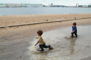 Twins in St. Petersburg, gumboots in puddle, beach and waterfront in back.