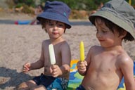 Twins, hats, ice cream on beach.