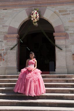 Rose Mexican girl, her 15 year celebrations (fiesta de quince anos) dressed in rose wedding dress, on steps of San Pedro church in Mitla, Oaxaca..