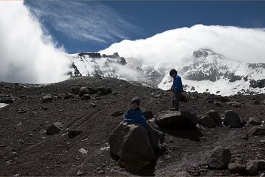 Twin boys raise arms, Chimborazo glacier and blue skies.