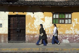 Morning sun on orange house, two young ladies walk by, Cajamarca, Peru.